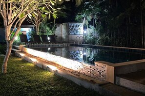 An outdoor swimming pool with a brick border, surrounded by grass and plants, and a bench area with chairs. - Moubillow Resort (Krabi)