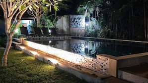 Ein Schwimmbecken bei Nacht mit Ziegelbordurand, umgeben von üppigem Grün und einer Zierwand.
