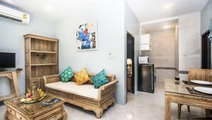 Ein Wohnzimmer mit einem Holzsofa, einem Couchtisch, einem Esstisch und einer Küchenzeile.