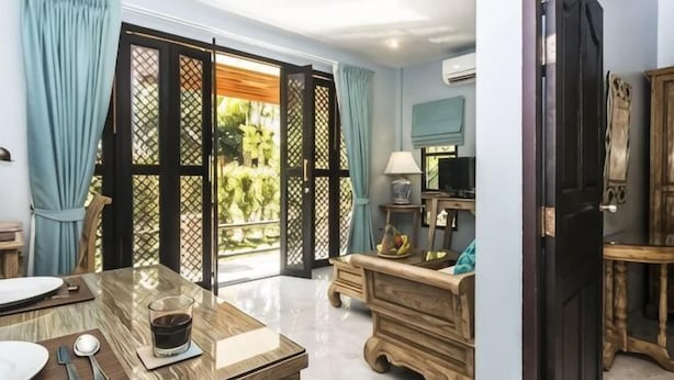 Ein Zimmer mit Esstisch, Fernseher, einem Holzschrank und einer Glastür zum Balkon.
