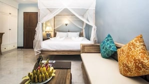 Ein Schlafzimmer mit Himmelsbett, Nachttisch mit Obstschale und einer Couch mit gemusterten Kissen.