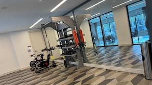 Un gimnasio con equipo de ejercicio, una bicicleta estática y un amplio ventanal con vistas a palmeras.