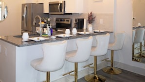 Una cocina moderna con armarios blancos, electrodomésticos de acero inoxidable y una zona de bar con taburetes blancos.