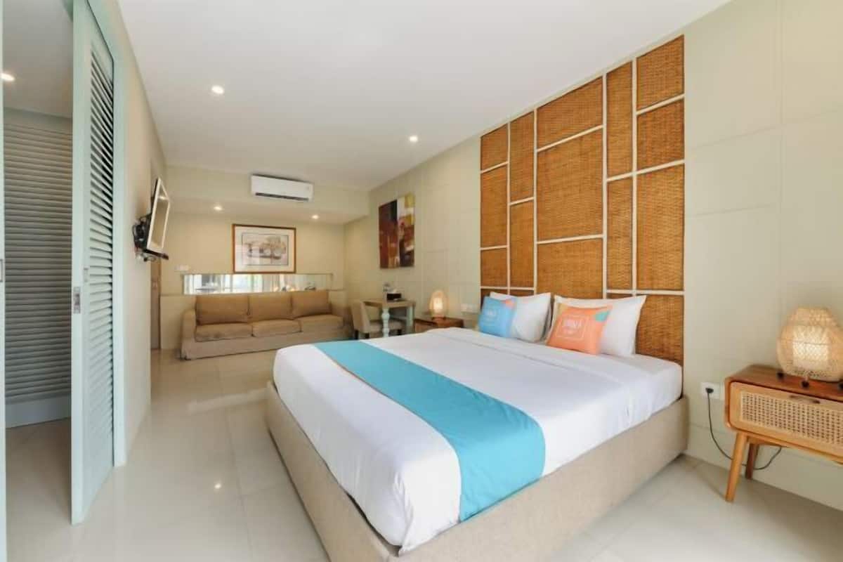 A modern hotel room with a large bed, a sofa, a small table, and a wall-mounted TV.