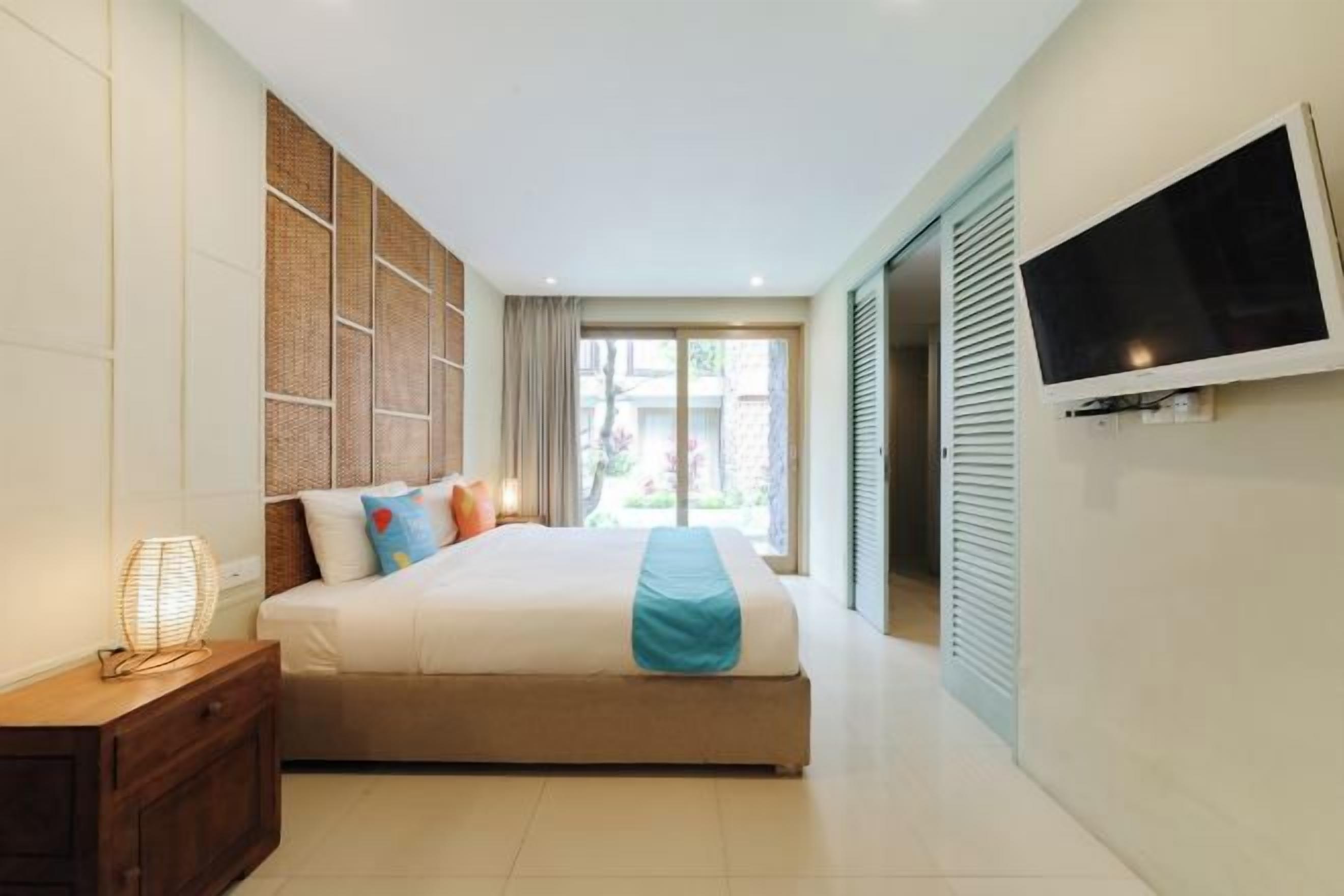 Hotelkamer met een bed, een aan de muur bevestigde televisie, een raam met gordijnen en een deur naar een balkon.