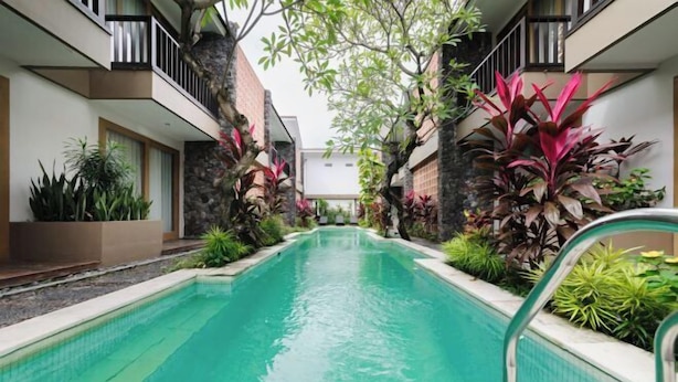 A swimming pool with a clear water surface, surrounded by plants and a stone wall. - Sans Vibes Astana Residence Seminyak (Bali)