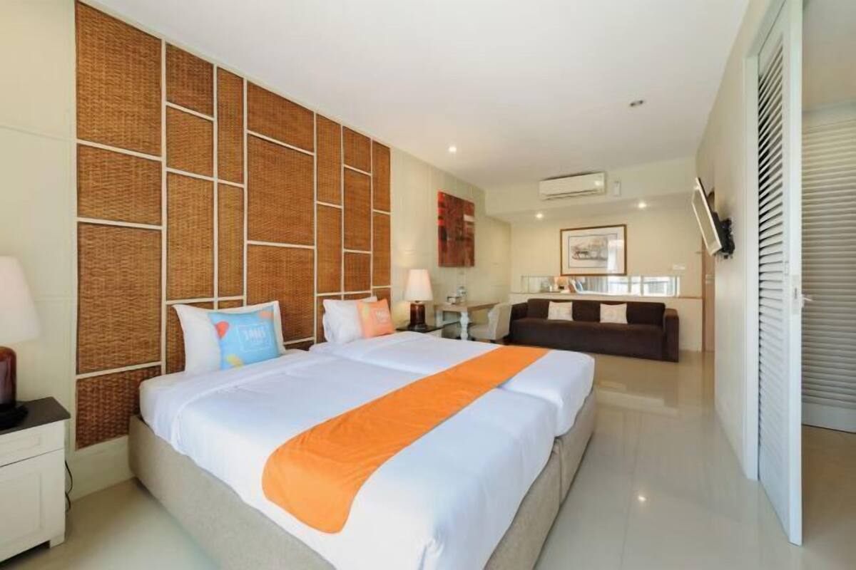 A hotel room with a large bed, a sofa, a desk, and a wall with a woven pattern.
