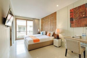 A hotel room with a bed, desk, chair, and a large window with a view. - Sans Vibes Astana Residence Seminyak (Bali)