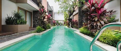 A swimming pool with a clear blue water surface, surrounded by lush greenery and modern architecture.