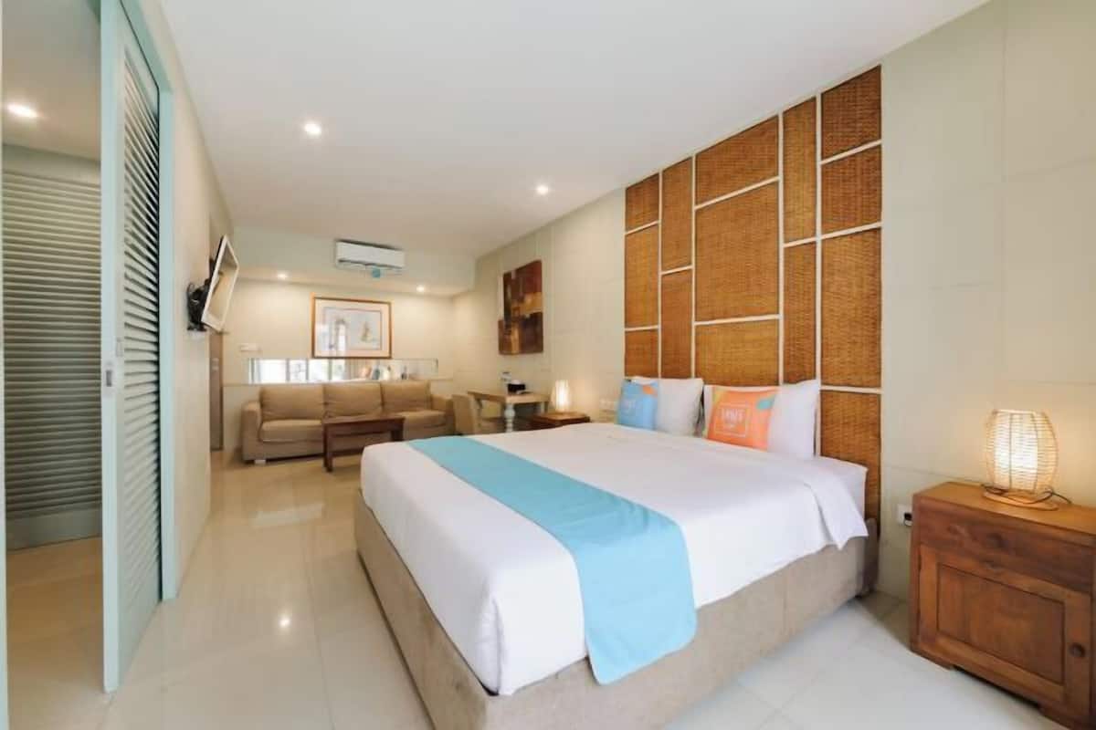 A hotel room with a large bed, a sofa, a wooden headboard, a nightstand, and a wall-mounted TV.