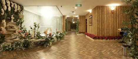 A hotel lobby with a wooden floor, a reception desk, and a wall decorated with flowers and plants.