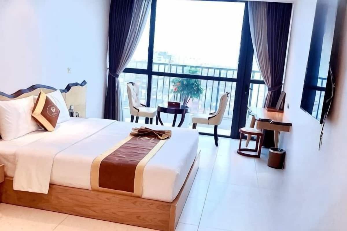 A hotel room with a bed, a small table, two chairs, a TV, and a balcony with a view.