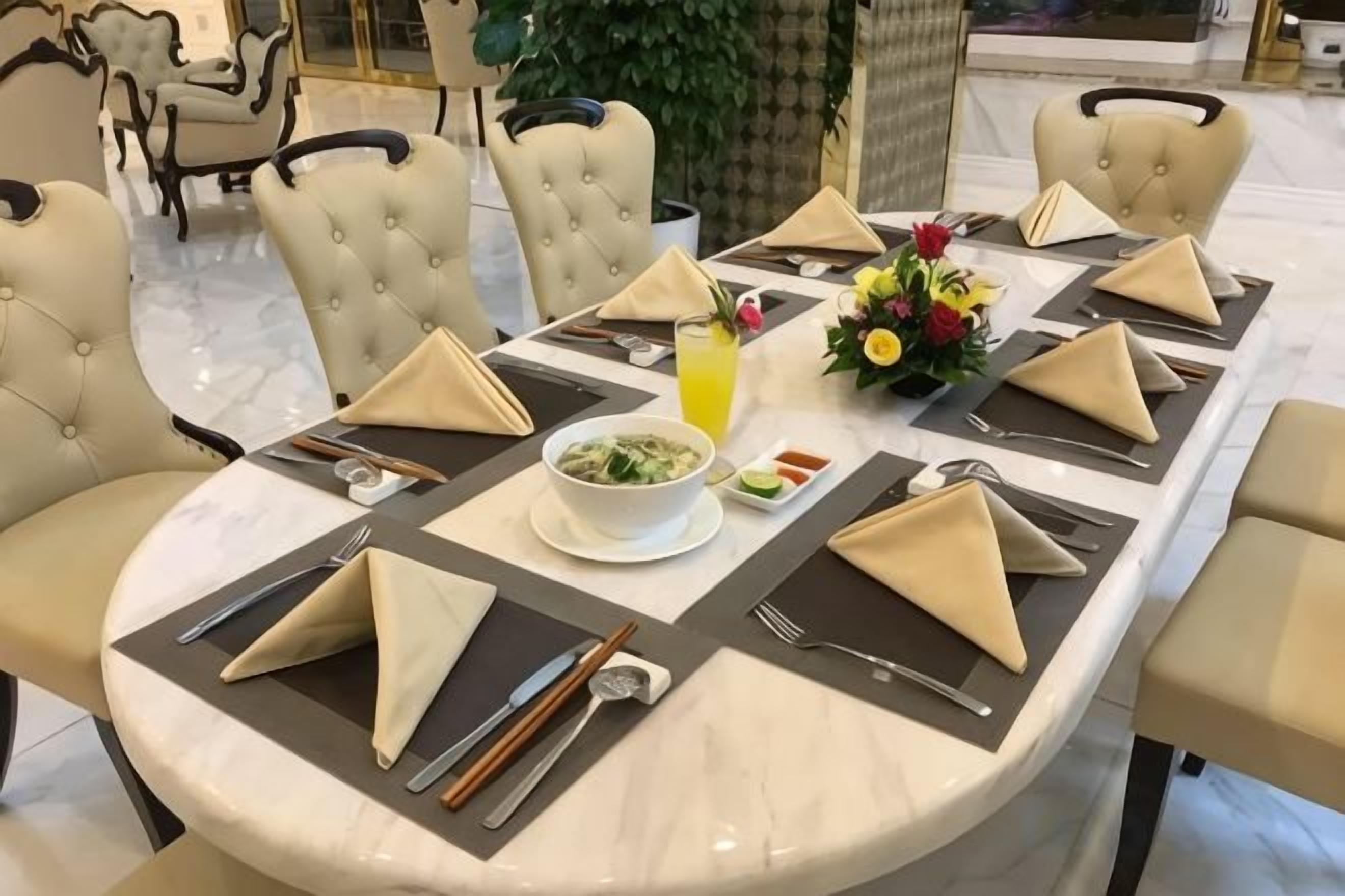 Una mesa de comedor redonda dispuesta con servilletas beige, cubiertos y un tazón de comida, rodeada de sillas tapizadas.
