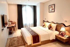 Une chambre d’hôtel comprenant un lit, une table de chevet, une lampe, un bureau, une chaise et une grande fenêtre avec des rideaux.