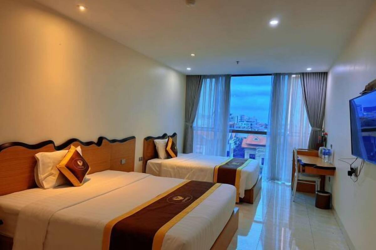A hotel room with two beds, a desk, a TV, and a view of the city.