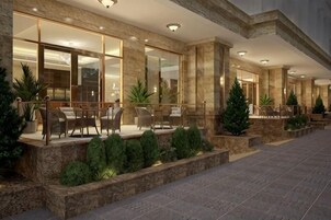 Exterior de un hotel con asientos al aire libre, jardineras de piedra y una entrada bien iluminada.