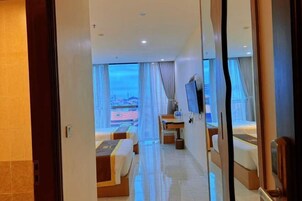 Habitación de hotel con cama, escritorio, silla, televisión y un amplio ventanal con vista a la ciudad.