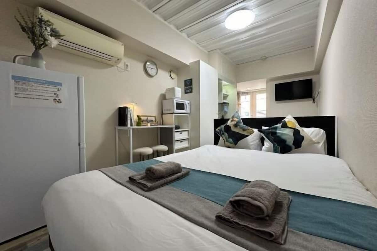 A hotel room with a bed, a desk, a microwave, a television, and a clock on the wall.