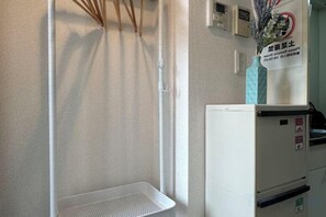 A corner of a room with a white wall, a white shelf, and a white refrigerator.