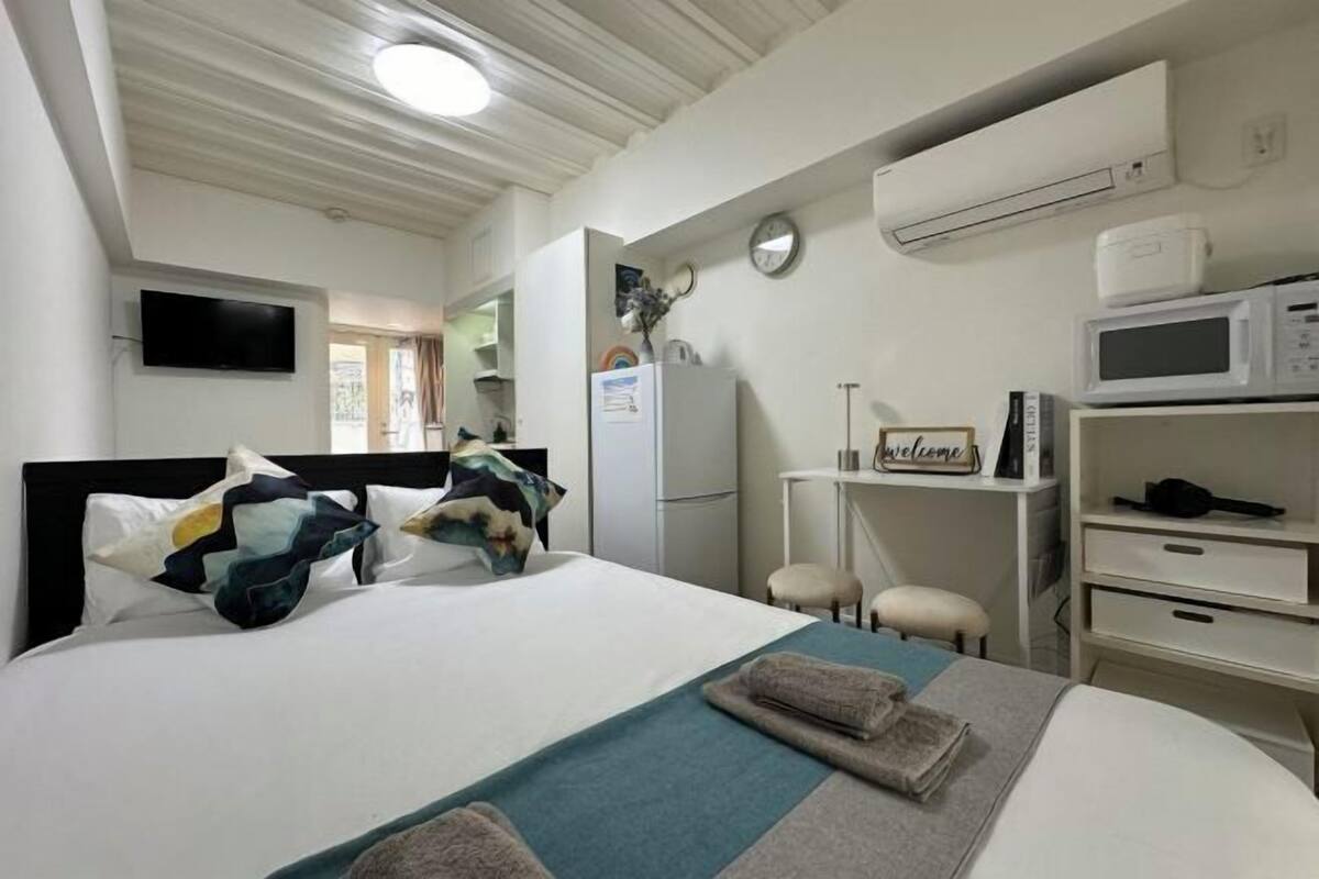 A hotel room with a bed, a desk, a microwave, and an air conditioning unit.