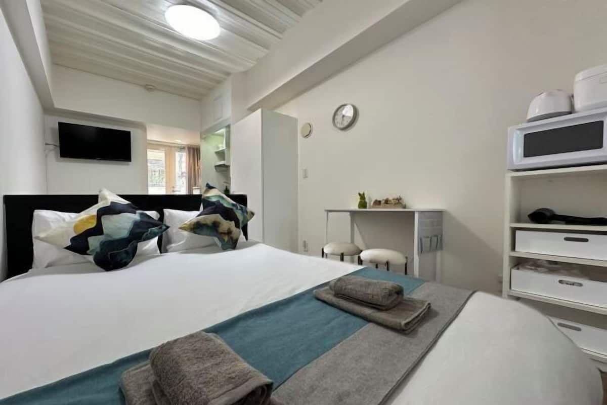 A hotel room with a bed, a desk, a chair, a TV, and a microwave.
