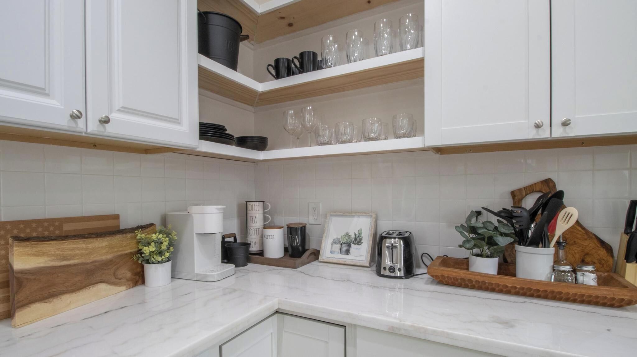 Una cocina con armarios blancos, encimera de mármol, cafetera, tostadora y diversos utensilios de cocina.