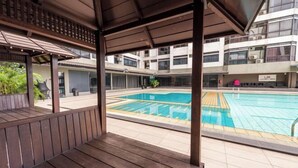A covered outdoor area with a pool, wooden deck, and a view of a multi-story building in the background. - Fahrenheit88-Ancient Loft House ( Japan Theme ) (Kuala Lumpur)