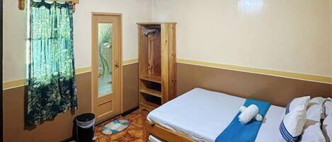 A small room with a single bed, a wooden wardrobe, a door, and a patterned floor.