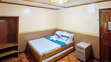 A small bedroom with a bed, a wooden wardrobe, a desk, and a door.