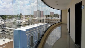 A corridor with a curved glass wall offering a view of a cityscape, including buildings and a clear sky. - Mérida Centro Retreat w/ Outdoor Pool, Garden Views & Walkable Cultural Hotspots (Mérida)
