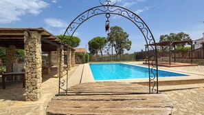 A swimming pool with a stone patio and a pergola structure.