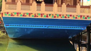 Un bote tradicional con elaboradas tallas de madera y base azul, adornado con un motivo floral decorativo a lo largo del costado.
