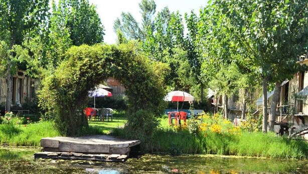 Un jardín tranquilo con un estanque, un muelle de madera y un paraguas rojo y blanco.