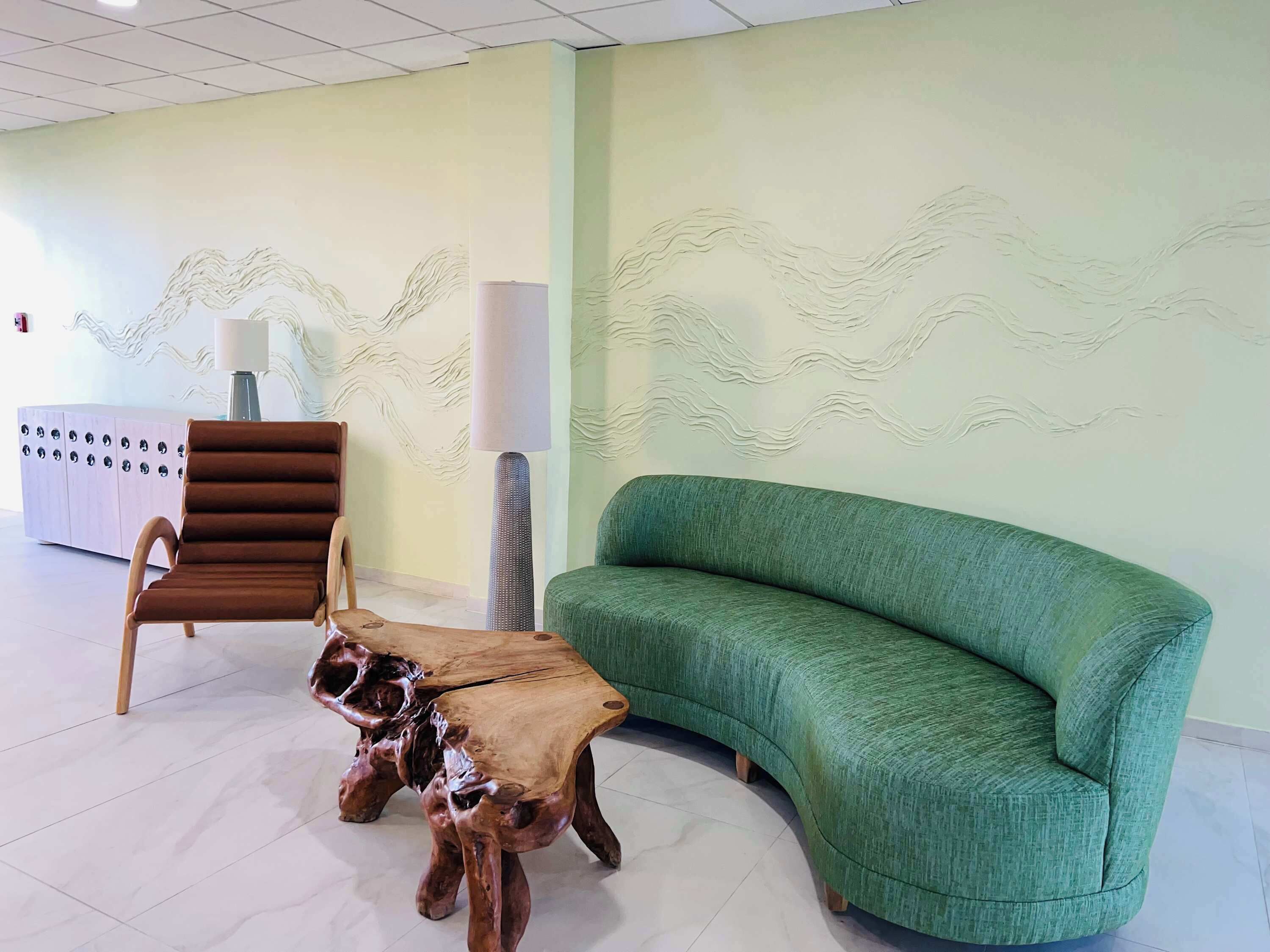 Ein modernes Interieur mit einem grünen Sofa, einem Holztisch, einem braunen Ledersessel und einem Schrank mit runden Griffen.