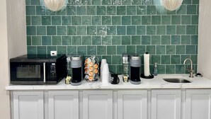 Una cocina con salpicadero de azulejos verdes, microondas, cafetera, hervidor y un lavabo.