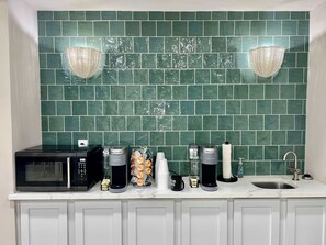 A kitchen with a green tiled backsplash, a microwave, a coffee maker, a kettle, and a sink. - Blue Bliss Beachfront Condo (Galveston)