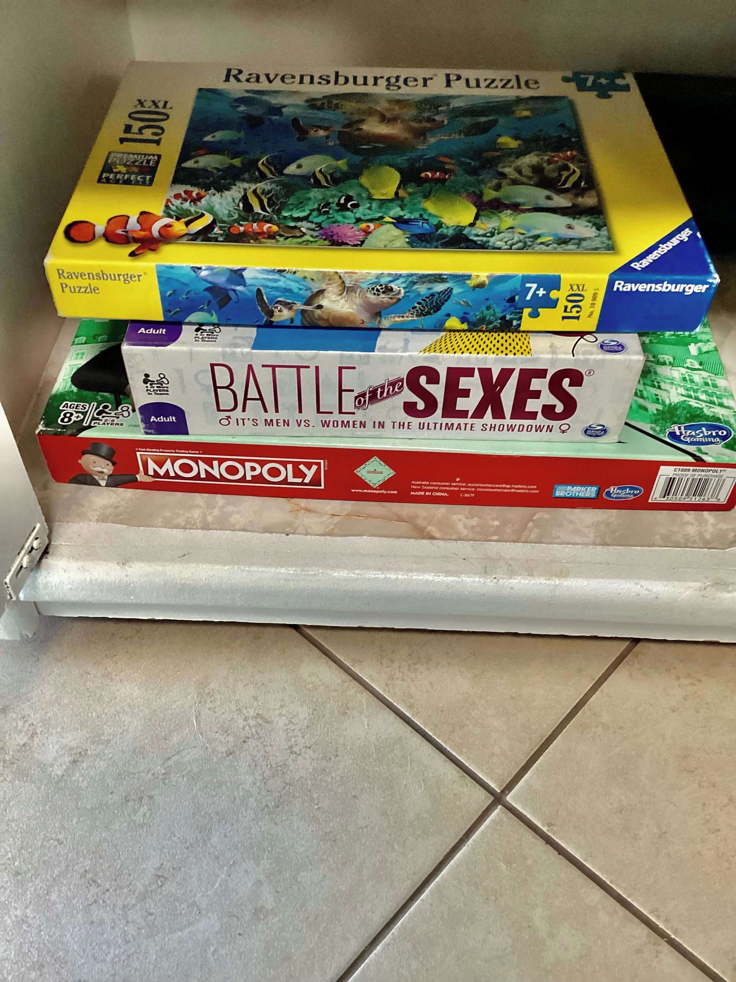 A stack of board games including Ravensburger Puzzle, Battle of the Sexes, and Monopoly.