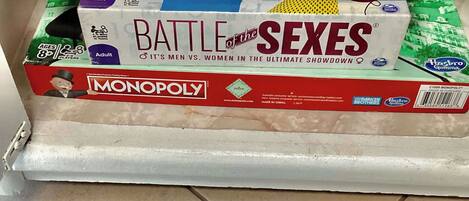 A stack of board games including Ravensburger Puzzle, Battle of the Sexes, and Monopoly.