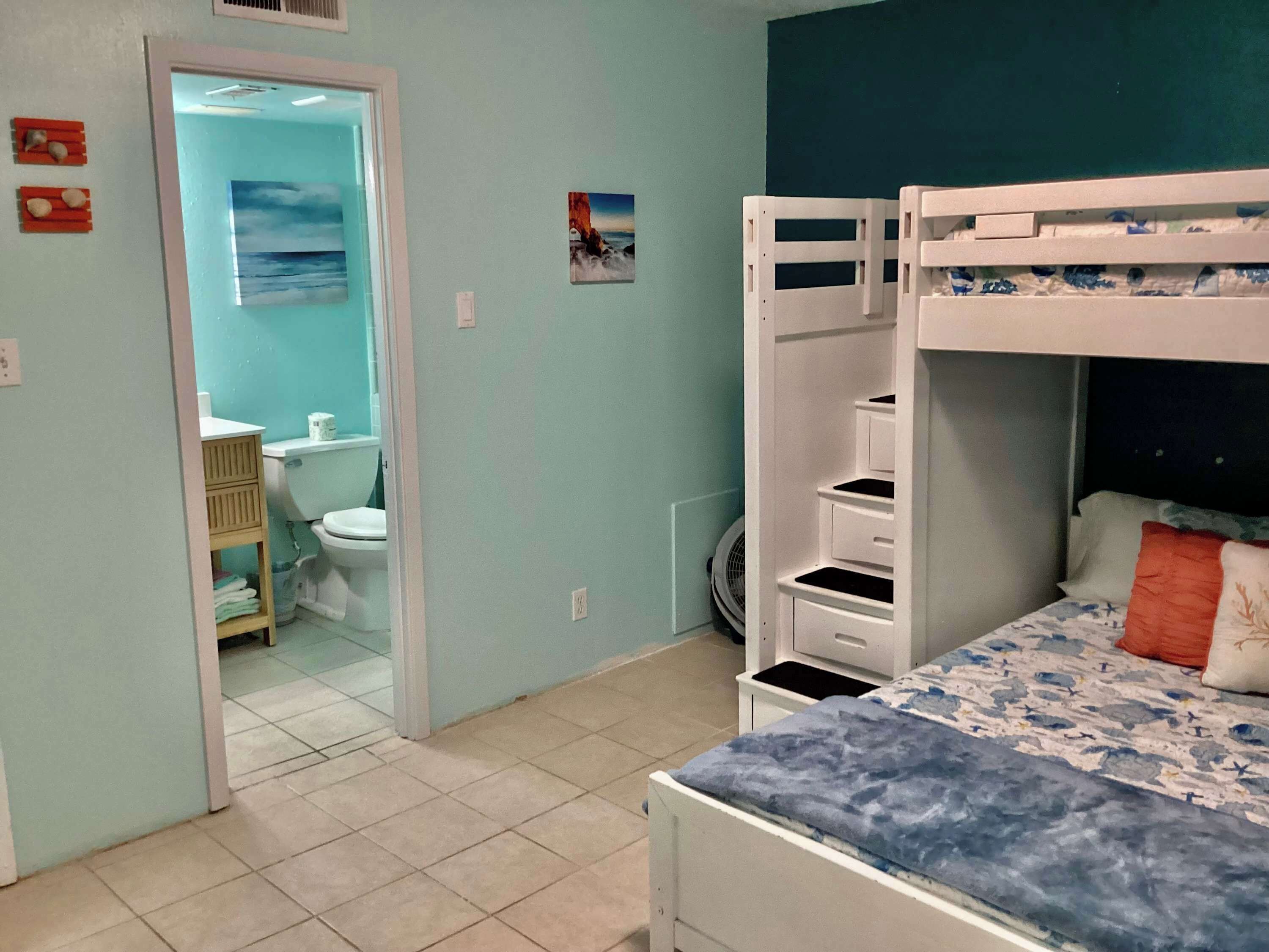 Une chambre avec des lits superposés, une salle de bain avec des toilettes et un lavabo, et une vue sur la mer.