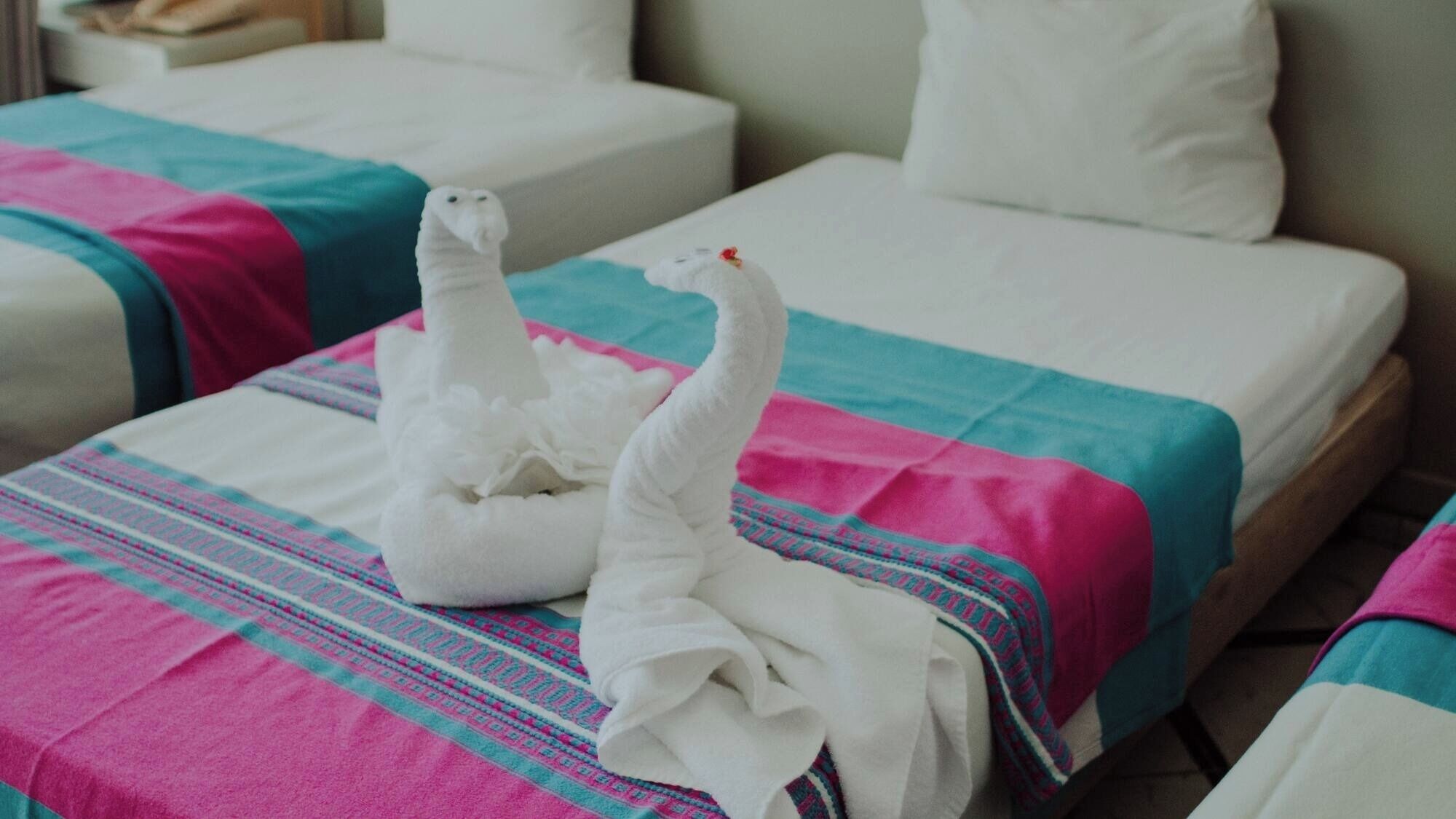 A hotel room with two beds, each with a colorful bedspread and white pillows.