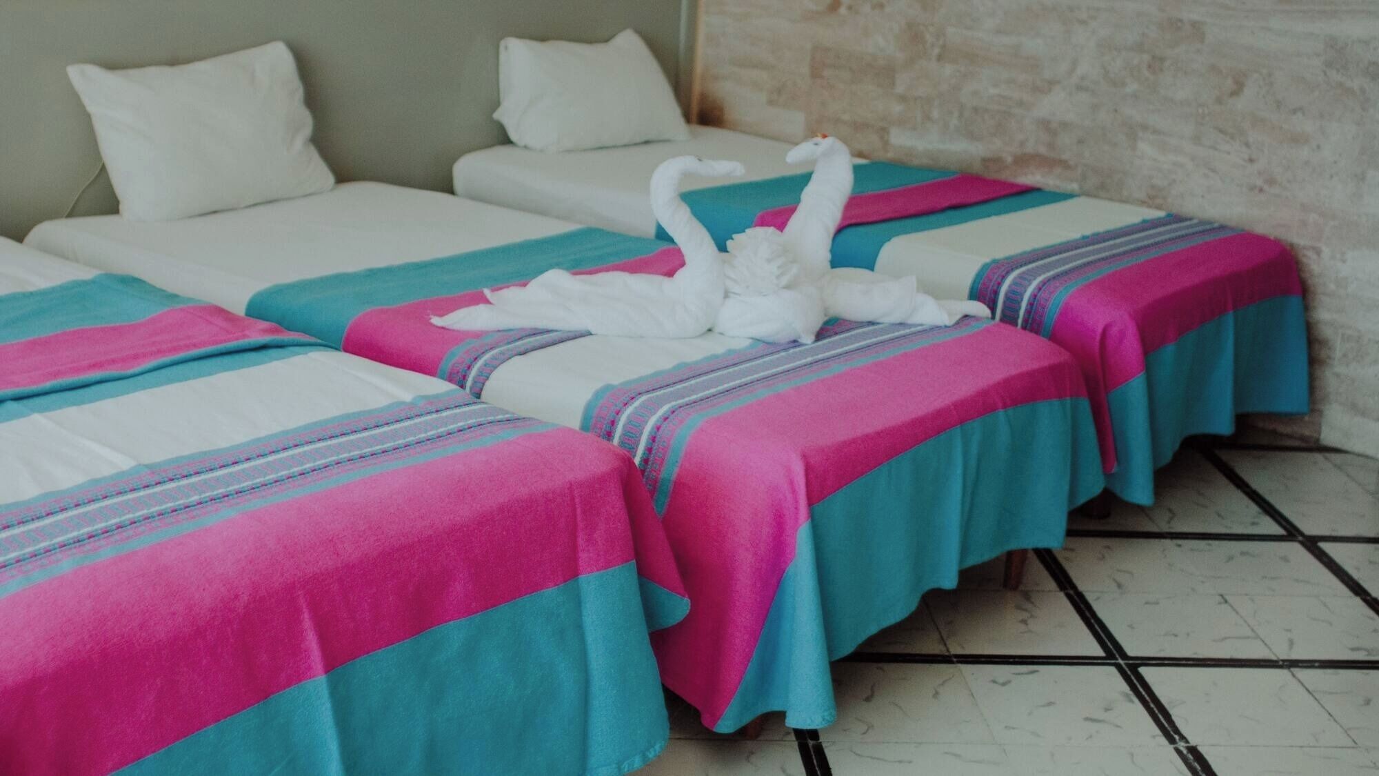 A hotel room with two beds, each with a pink and blue striped bedspread and white pillows.