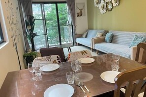 Un comedor con una mesa dispuesta para cuatro, un sofá al fondo y un ventanal con cortinas.