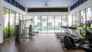 Une salle de sport équipée de tapis de course, d’appareils d’exercice et de grandes fenêtres donnant sur une piscine et un espace verdoyant.