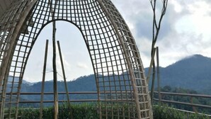 Une structure en bambou, avec un motif en forme de grille, qui offre une vue sur un jardin luxuriant et des montagnes lointaines.