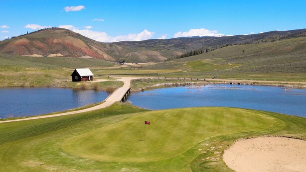 A golf course with a pond, a small building, and rolling hills in the background. - Cozy Slope Slide Granby Condo (Granby)