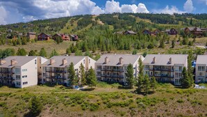 A cluster of multi-story buildings with balconies, set against a backdrop of a mountainous landscape with dense forests. - Cozy Slope Slide Granby Condo (Granby)