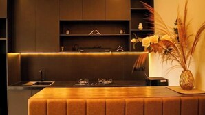 Une cuisine moderne dotée d’un îlot central intégré, de meubles de rangement aux couleurs sombres et d’un éclairage d’ambiance chaleureux.