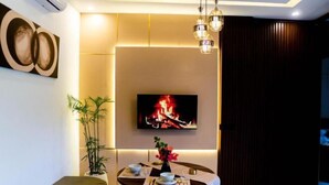 Un salon moderne avec un téléviseur fixé au mur, une table à manger ronde agrémentée d’un vase de fleurs et une grande plante en pot.