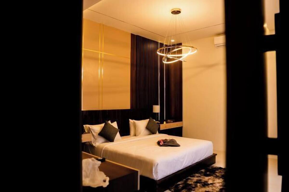 A modern hotel room with a large bed, a hanging light fixture, and a dark wooden headboard.