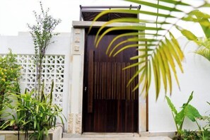 Una entrada moderna con una puerta de madera oscura, paredes blancas y una valla ajardinada.